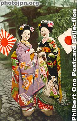 Two Patriotic Maiko. To cheer up the soldiers on the front line, pretty and smiling maiko (apprentice geisha) often appeared on postcards for military mail. This card was postmarked Aug. 1940 from Shizuoka city. It was not addressed to a soldier though.
Both women are maiko and not full-fledged geisha yet. The sleeves of a maiko's kimono reaches toward the ground as you can see here. (The sleeves of a geisha is shorter.) The kimono design is also more colorful and gaudy. Maiko also wear clogs called pokkuri. They are wedged at the front, so if you are not careful, you can trip forward. Geisha do not wear pokkuri.
Keywords: japanese vintage postcards nihon bijin women beauty geisha maiko woman kimono flag