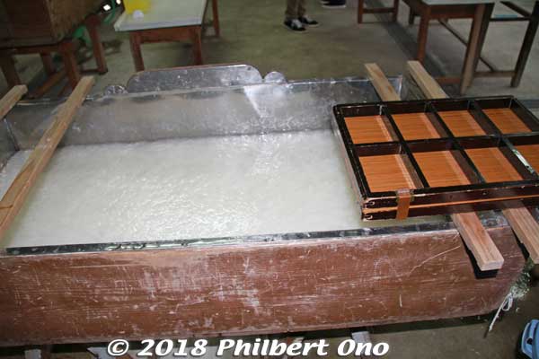 A large vat (sukifune) filled with washi fibers floating evenly in the water. The fibers are mixed in with a plant-based adhesive so they don't sink to the bottom and they also cling together to make the paper. 
A wooden mold (keta 桁) to make eight postcards on the right. Kurotani washi bills itself as Japan's strongest paper. In the 1920s, Kurotani washi was tested for strength and was declared the strongest washi in Japan. I was told Kurotani's kozo has longer fibers than other species so the paper is stronger.
Keywords: kyoto ayabe Kurotani washi paper making