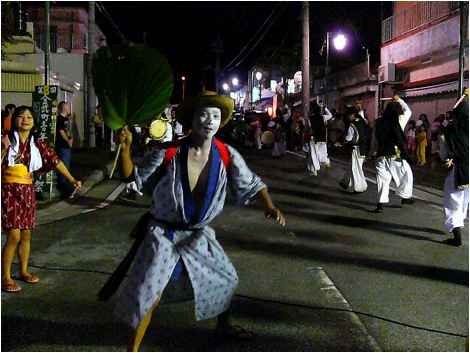 Here the Buffoon (called Gajangani) can be seen going in the opposite direction of all the other male dancers and waving a banana leaf. Some clowns carry bottles of sake and try to get bystanders to drink with them.
Photo copyright 2009 Michael Lynch.
Keywords: okinawa kin eisa obon dance dancing 