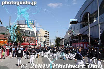 Streamers from part poppers blown by the wind get caught in the power lines. The best spot to take pictures here is occupied by a police/press grandstand seen on the right with the red and white curtain. 
Keywords: osaka kishiwada danjiri matsuri festival floats 