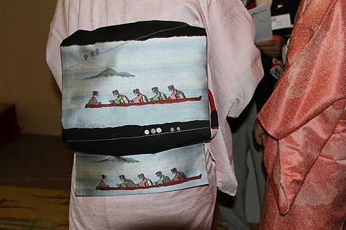 The back of her kimono obi sash has a design featuring rowing geisha.
