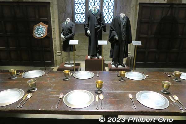 Tableware in the Slytherin section with their robes displayed behind.

