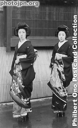 Geisha Pair Outside Geisha House. These two geisha know how to pose for the camera. It looks like Kyoto. You can tell that they are geisha because of the shorter kimono sleeve, subdued kimono design (mostly black), and their clogs (for rainy weather).
Keywords: japanese vintage postcards nihon bijin women beauty geisha maiko woman kimono