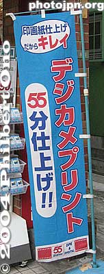 55-min. Photos
The term "one-hour photo" was once popular, but it seems "55 minutes" has taken over. Below the number "55" is the kanji for "fun" or minutes. Below that is "shiage" meaning "finished in." Thhe red katakana characters on the right says "Digital camera prints."
