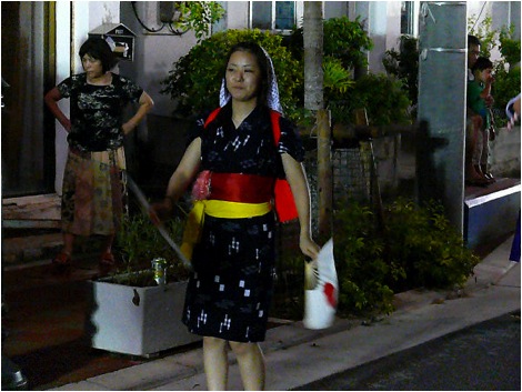 Eisa dancing is performed on the streets at night in every village on Okinawa during the three days of Obon, late in August. Here a young lady dressed in traditional Okinawan yukata (an informal kimono) marches while waving Rising Sun paper fans.
Photo copyright 2009 Michael Lynch.
Keywords: okinawa kin eisa obon dance dancing 