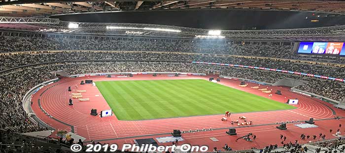 It's an oval-shaped stadium with a track and field and partial, fixed roof. The track and field had taiko drums and kanto paper lantern poles on both ends.
The seats have a random mosaic design in shades of green, 
Keywords: tokyo shinjuku olympic national stadium