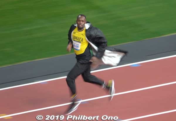 Usain Bolt runs to his position on the track. It was a cold evening so the runners wore overcoats before the race.
